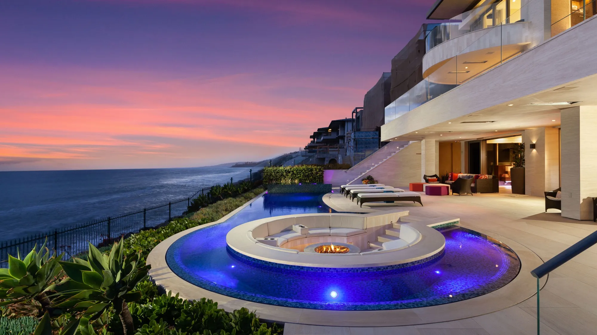 Oceanfront luxury home with an infinity pool and fire pit at sunset