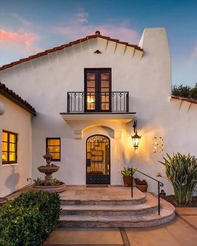 Spanish-style white stucco home with red tile roof, arched entry, and iron balcony
